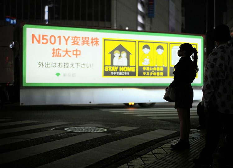 A pedestrian stands at Shibuya’s scramble crossing in late April as an illuminated truck passes by warning people of coronavirus variants and urging them to stay home.