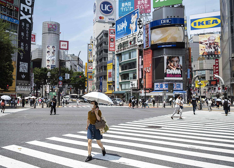 A woman protects herself from the sun and heat with an umbrella as she crosses a street in Tokyo on July 12.