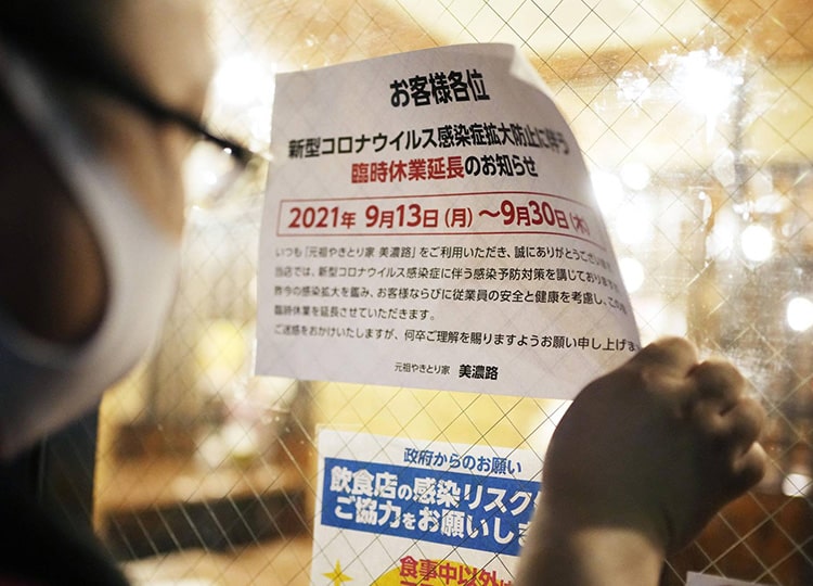 An employee of a roast chicken bar in Nagoya peels off a notice of temporary business suspension from its window on Sept. 30.