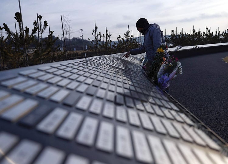 A man looks for the name of an acquaintance on the list of tsunami victims engraved on a cenotaph in Ishinomaki, Miyagi Prefecture, on March 11.
